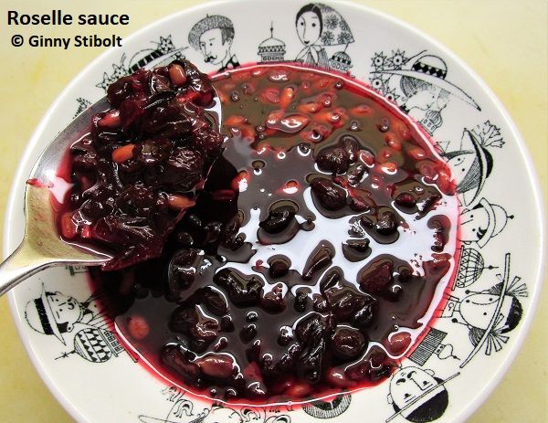 Photo of a bowl of what looks like cranberry sauce and a spoon being held with some of the sause. The rim of a white bowl has collection of black drawings of people's heads. All are wearing hats. There are drawings of some buildings or flowers between the people's heads.