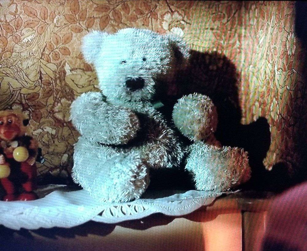 A teddy bear in front of a section of Walter Crane's "The Sleeping Beauty", a dense ochre-colored pattern of roses with small figures intertwined.