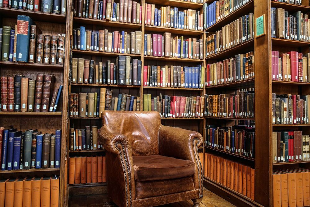 A leather chair in a nook between bookshelves. The books are from the Gladstone collection so they are 100+ years old.