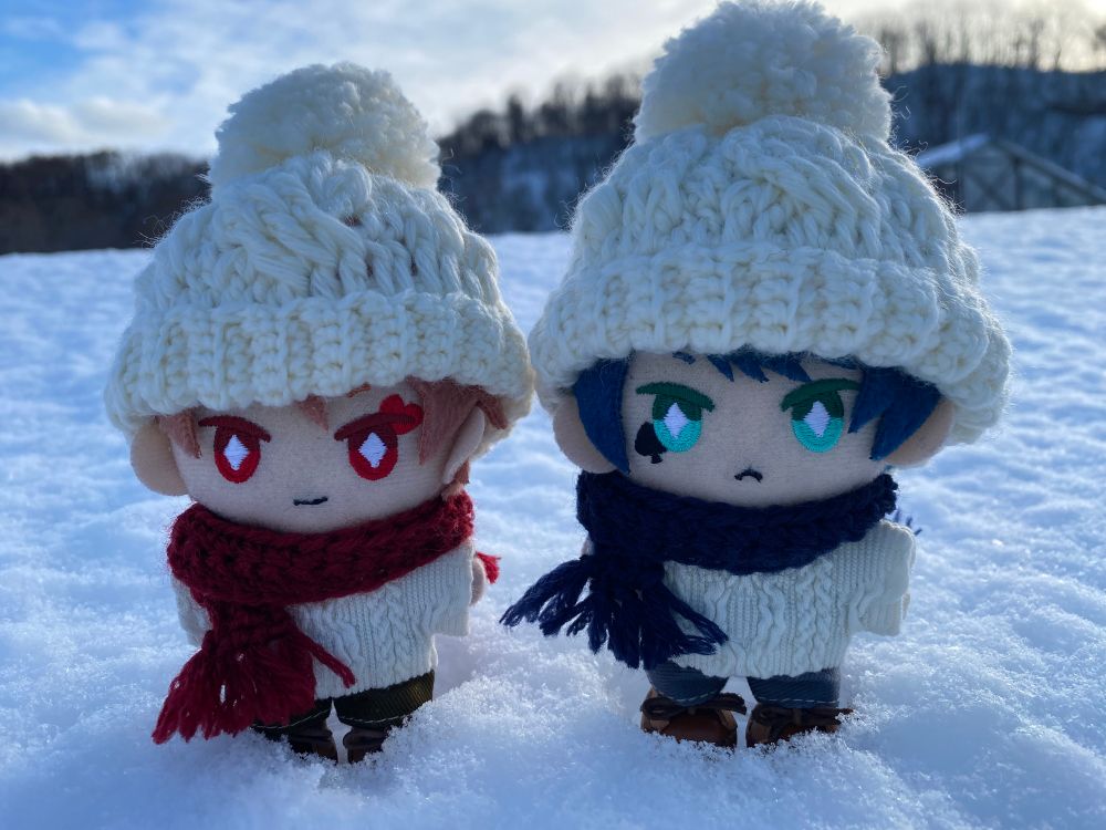 雪の中にニット帽やマフラーを付けた小さなぬいぐるみが2体立っている。