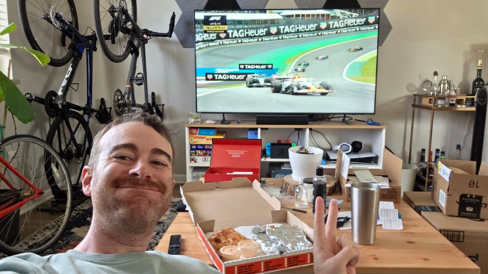 Me cheesing and throwing up a gang sign with leftover pizza on the table and F1 on the tv