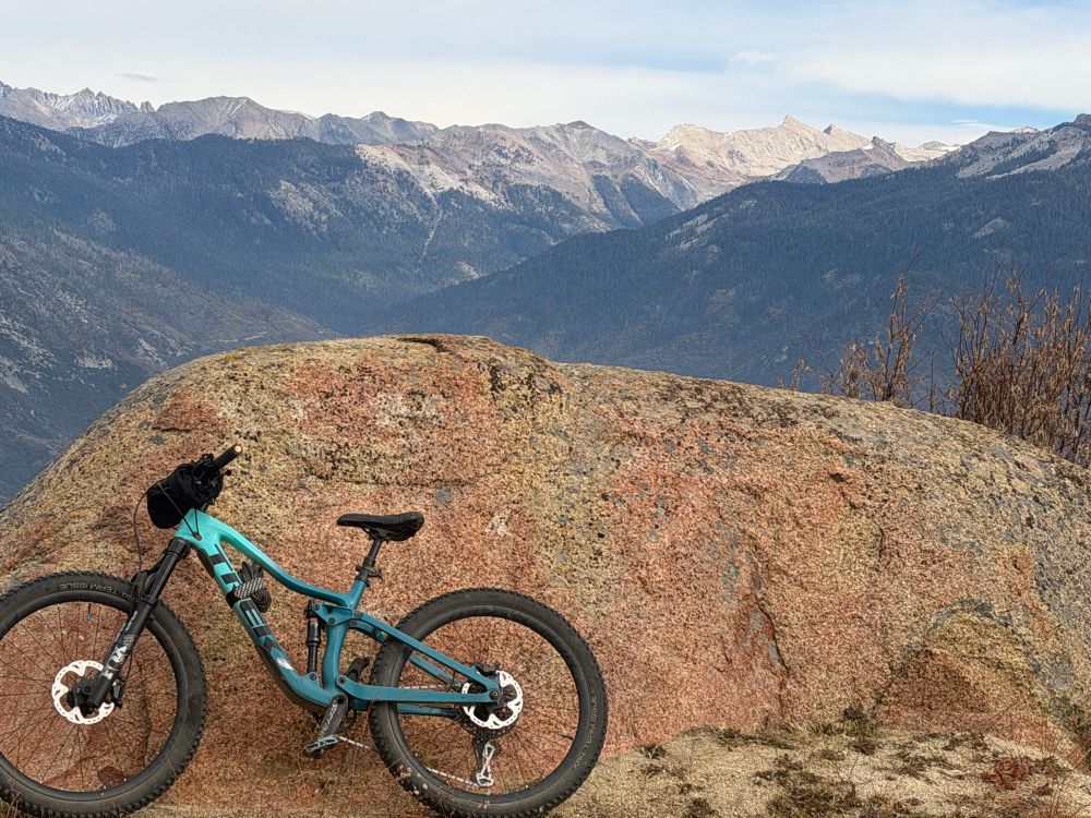 A blue mountain bike leaning against a reddish granite boulder with mountains in the background