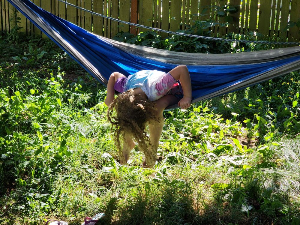 curly haired girl upside-down in a hammock 
