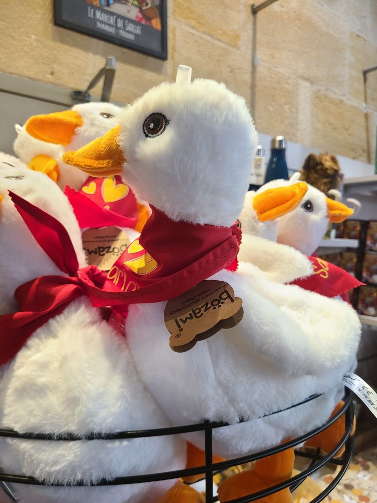 A flock of white soft geese toys in a shop display with red ribbons around their necks.