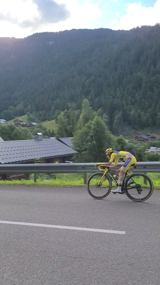 Pauline Ferrand-Prévot in yellow jersey rides from left to right in tuck position, in front of an alpine valley. 