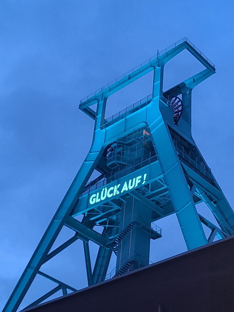Photo of the towering steel headframe of the German Mining Museum in Bochum. The sign reads Gluck Auf! (Good luck): a traditional German miners' greeting.