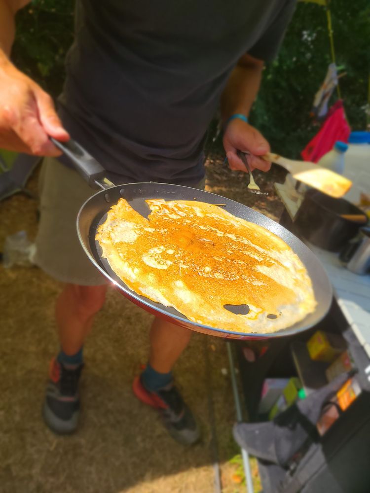 A pan with a crepe on it, held by a man in shorts.