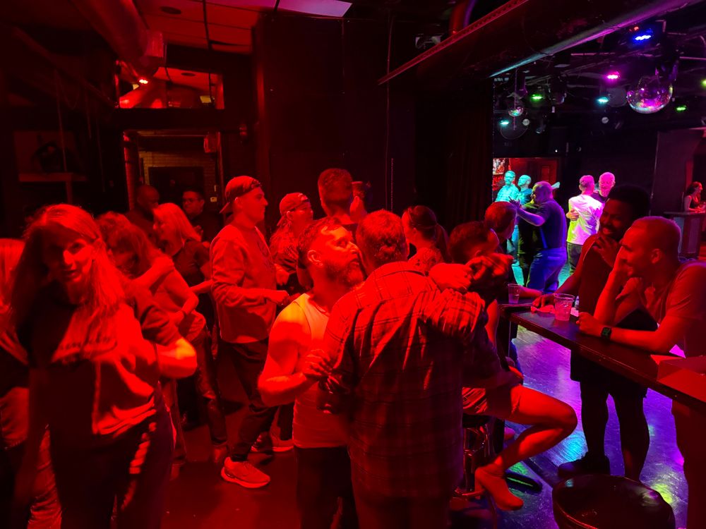 A group of young dancers socializing off the dance floor, some chatting, some hugging, and others listening. 
