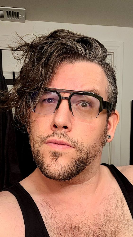 this user, a white masculine figure with chunky retrofuture glasses frames and a prominent chin with scruffy face and bedhead with a messy swoop of hair. 