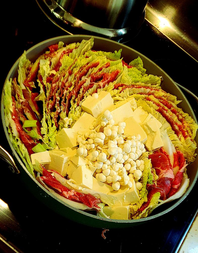 thinly sliced layers of meat and cabbage, arranged in a pan in a spiral radiating out from the center, which contains mushrooms, tofu and green onions. 