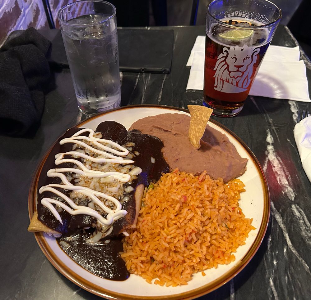 Plate of mole-drenched enchiladas with rice and beans, and a dark beer.