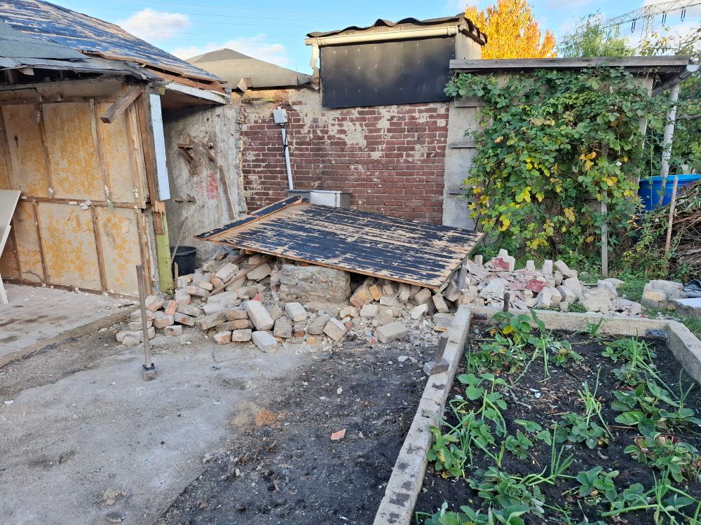 Der vordere Teil vom Anbau ist komplett in sich zusammen gefallen. Auf einem Haufen loser Ziegelsteine und Putz liegt der Teil vom Bretterdach, was den vorderen Teil abgedeckt hatte.