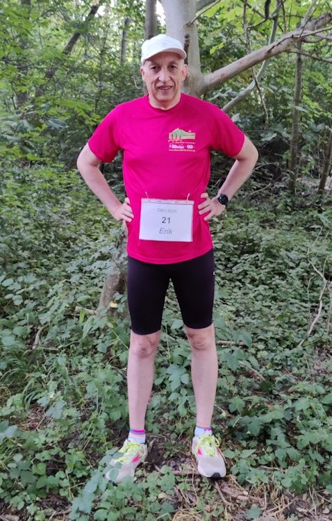 Ich stehe vor dem DBU 2025 vor einem Baum. Ich trage eine weiße Mütze, ein dunkelrosafarbenes Shirt, eine schwarze Hose und weiße Schuhe. Auf meinem Bauch ist die Startnummer 21 befestigt.