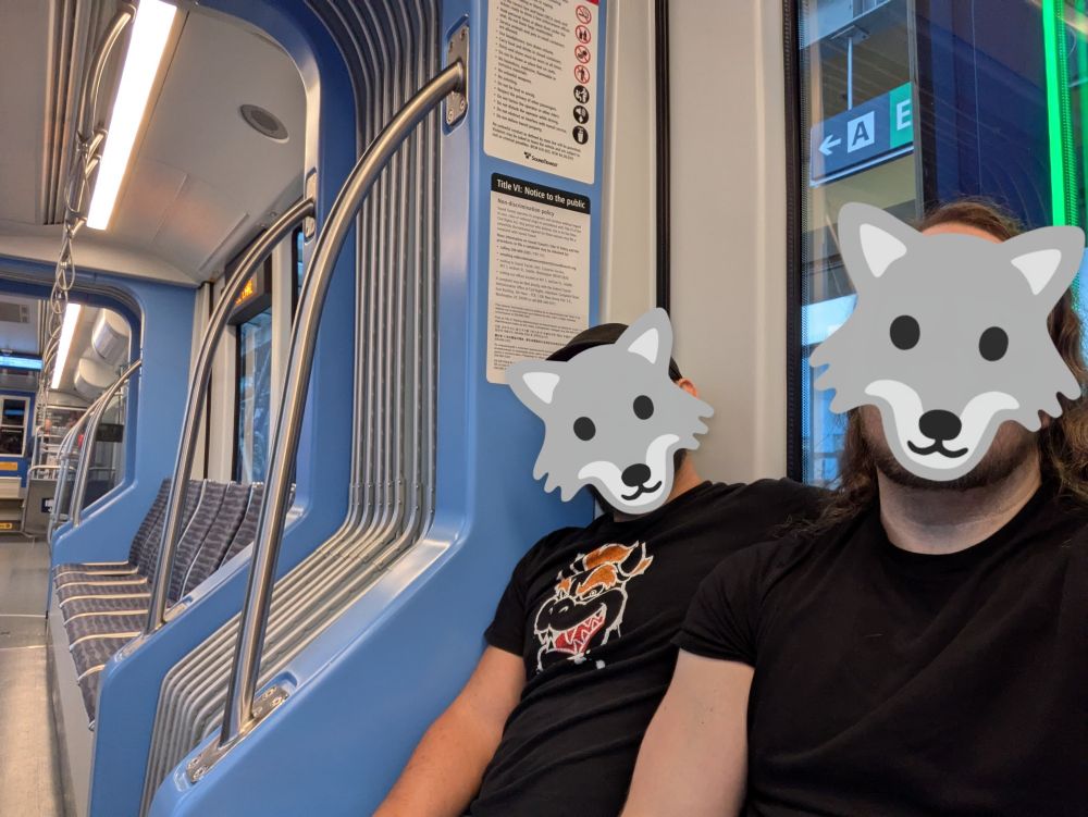 My husband and I sitting on a train, the local light rail. Our faces are obscured with wolf emoji 🐺🐺