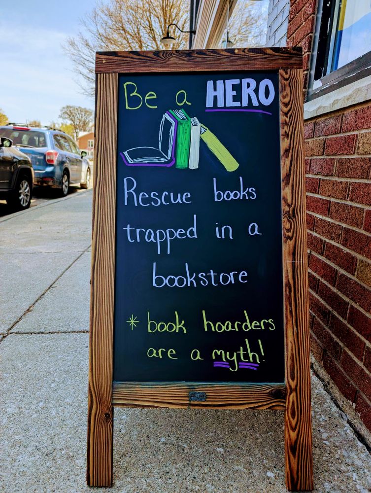 Become a hero for literature! This sidewalk chalkboard sign humorously frames book buying as a rescue mission: 'Be a HERO. Rescue books trapped in a bookstore,' and assures you, '* book hoarders are a myth!'"