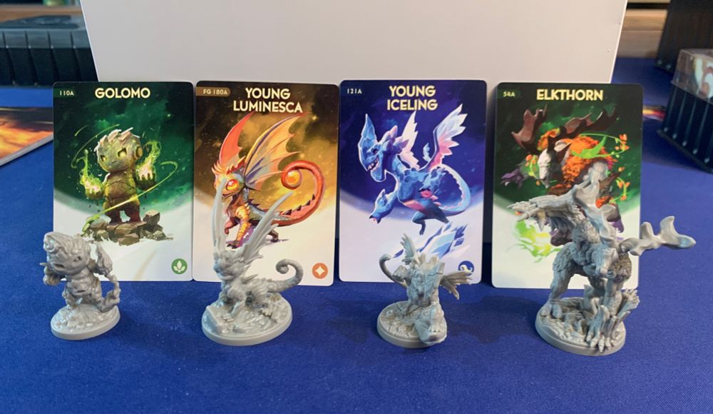 Mystling miniatures standing in front of their art cards: Golomo, Young Luminesca, Young Iceling, Elkthorn