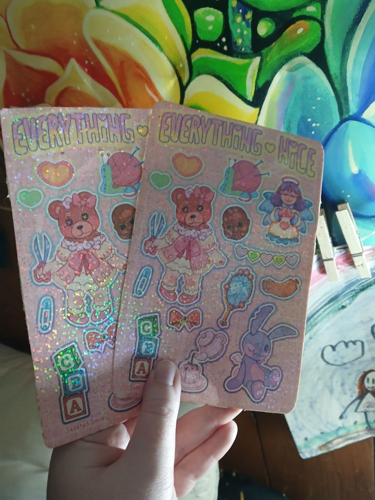 Sparkling sticker paper that says 'Everything Nice'. It is sweet, innocent themed with not-so-sweet intentions; i.e. a baby doll with it's head replaced with a torn teddy bear, holding scissors, a suspicious angelic three eyed doll, a shattered hand mirror with a faint hand print on the other side, a tea pot pouring blood, a baby doll head with a single eye, a single baby doll arm torn from its socket, an odd rabbit plush, and more.