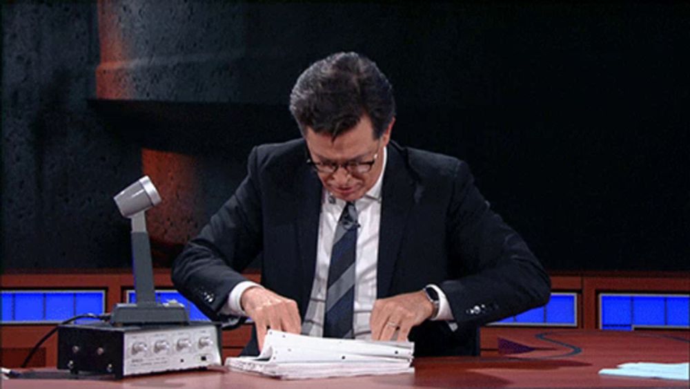 a man in a suit and tie sits at a table with a microphone