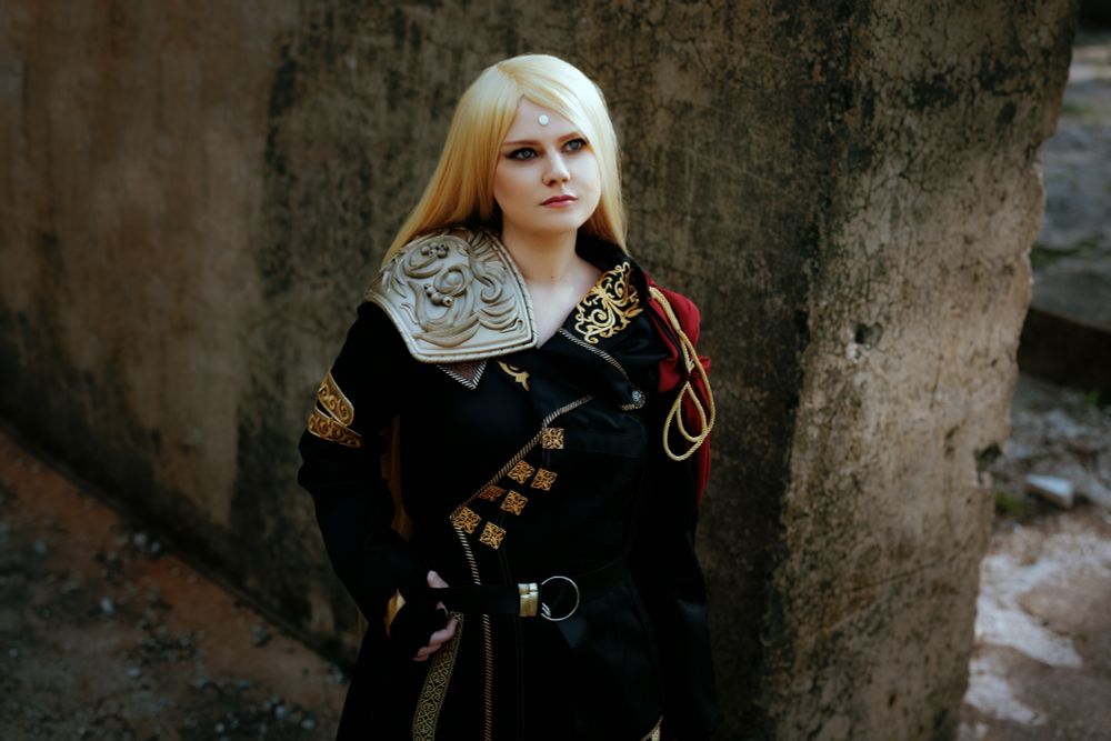 A cosplay of Zenos; cosplayer gazing up, wearing his black and gold endwalker outfit. The setting is rocky ruins.