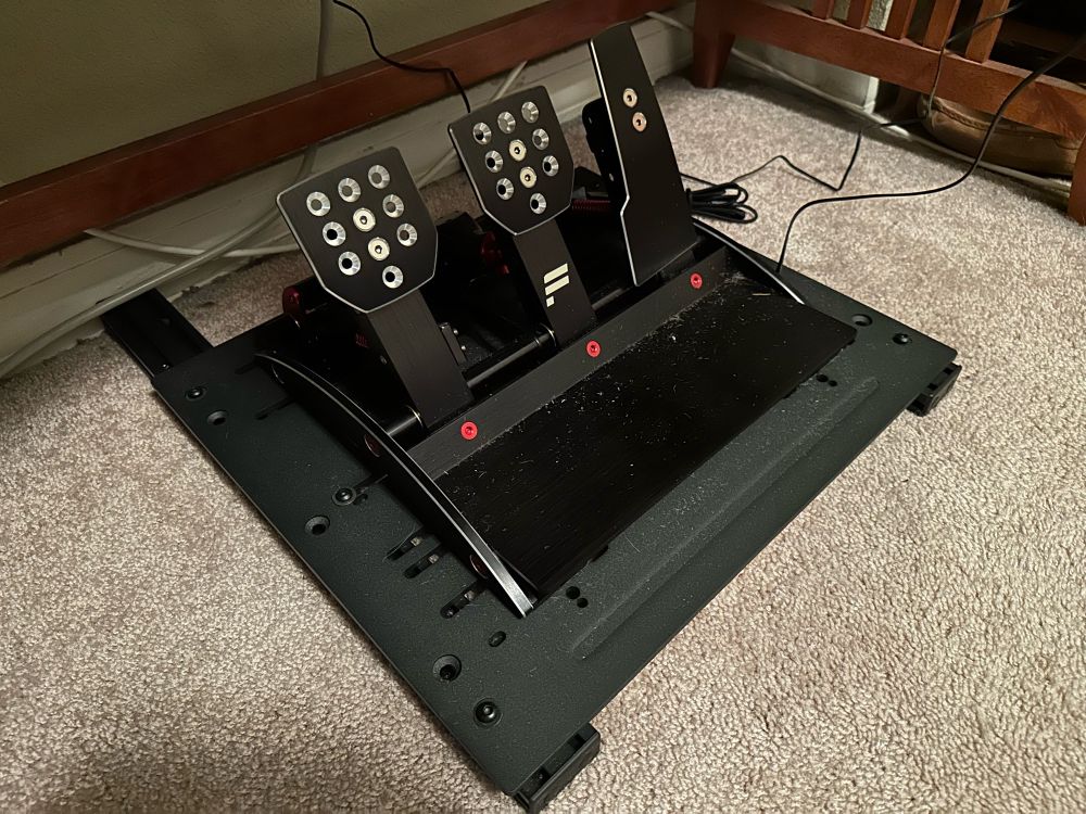 Sim racing pedals mounted on a movable platform.