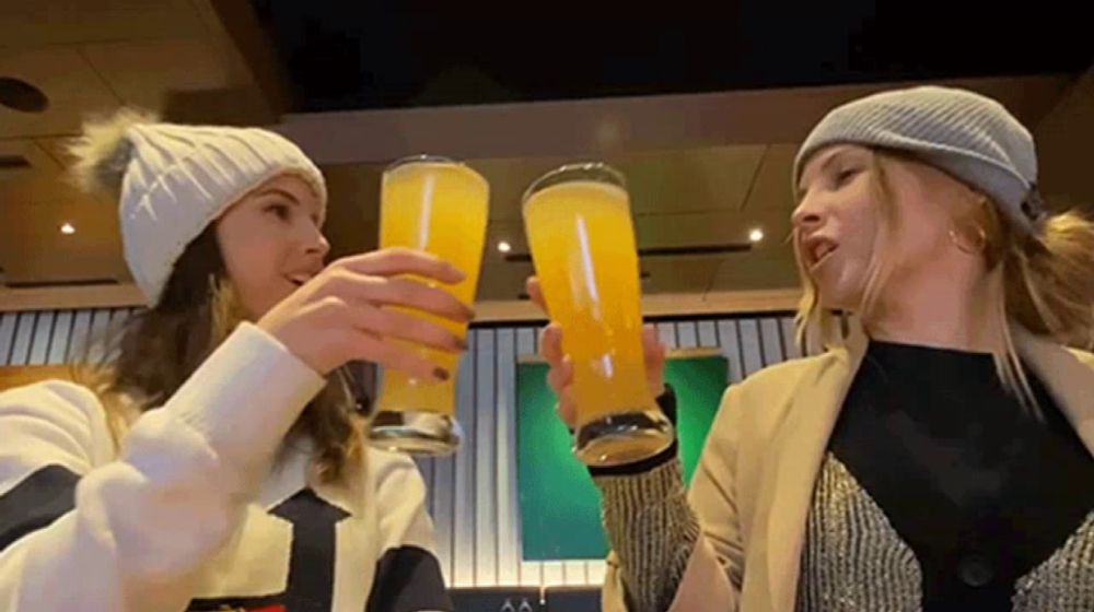 two women are toasting with glasses of beer in a restaurant .