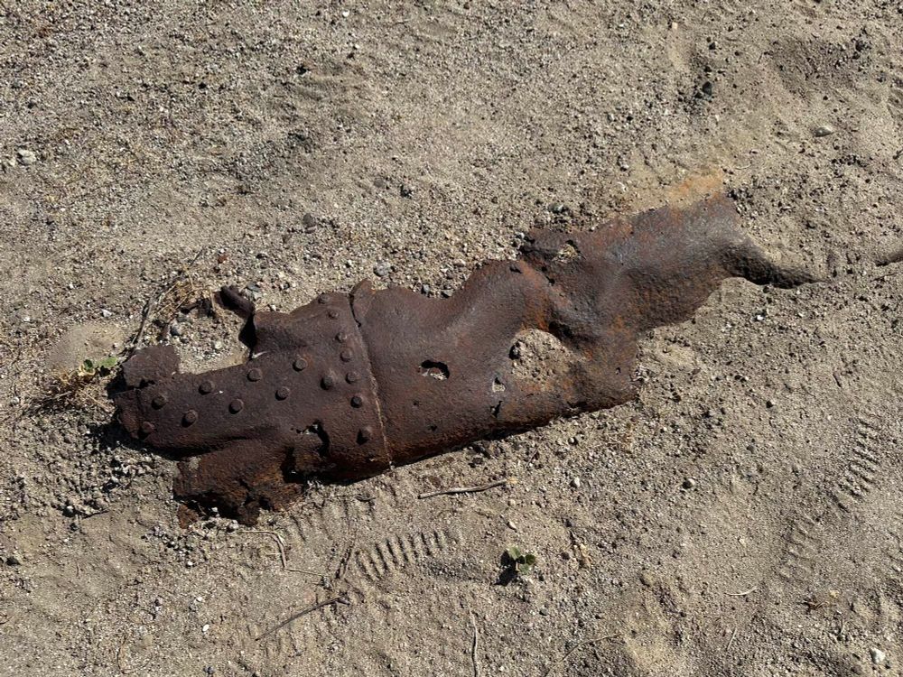 An old rusty something mostly buried in the sand