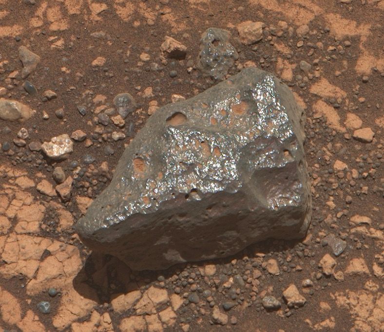 Rocks and sand. The main focus rock is shiny and gray with some dust in the nooks and crannies.

NASA/JPL-Caltech/ASU/Kevin M. Gill