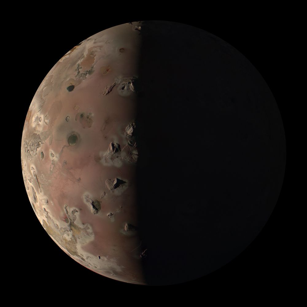 Io, a moon of Jupiter, at half phase and sunlit from the left. Tall volcanic mountains and lakes of lava dot the surface.