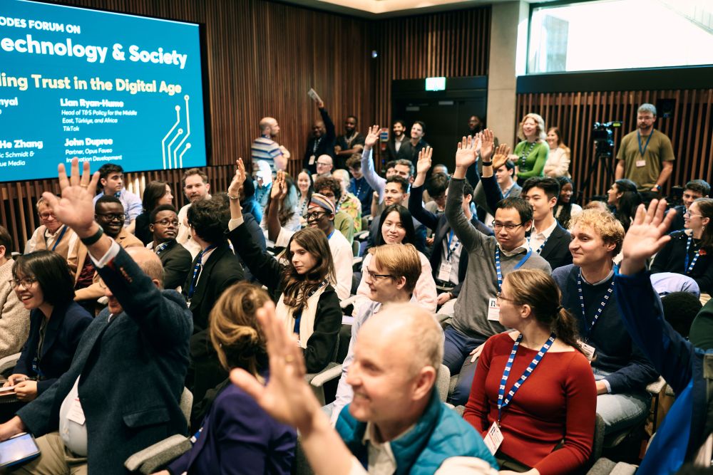 A room full of people shoot their hands up when asked if they have any questions. 