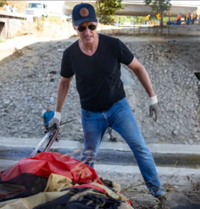 The image is a photo of Governor Gavin Newsom attacking the belongings of one of his constituents who has been driven away by the police ca. 2022
