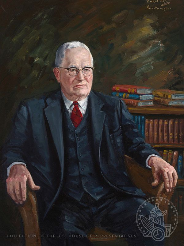 Portrait of a man in glasses with a red tie and blue three-piece suit.