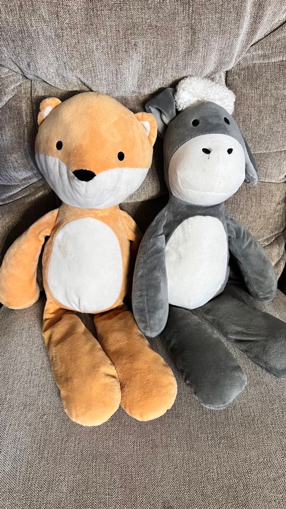 Image of two stuffed animals sitting on a rocking chair. Left is an orange creamsicle looking bear named “Dollar Milkl. The right is a gray and white Dokey named “$2 Juice.”
