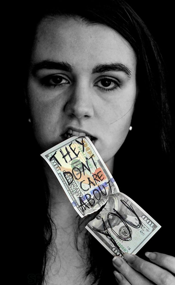 Self-portrait; staring into the camera with a fake $100 with the words "they don't care about you" written in Sharpie, in the mouth.