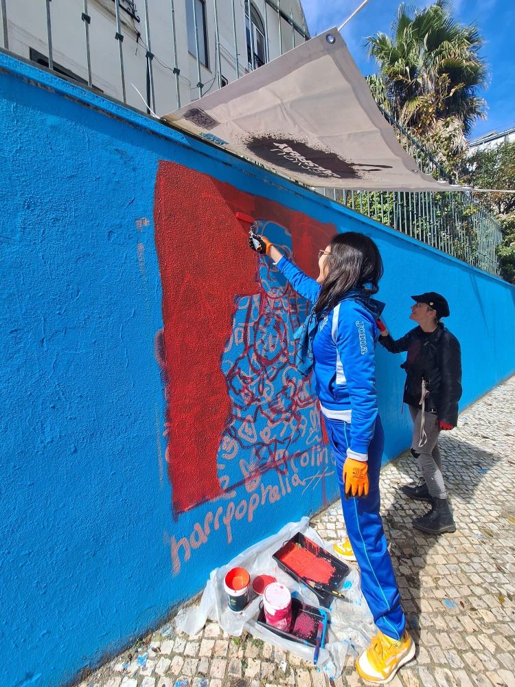 Myself and Bree paint the base coat of red on a blue wall under a small awning. The doodle grid can be seen in the background. 