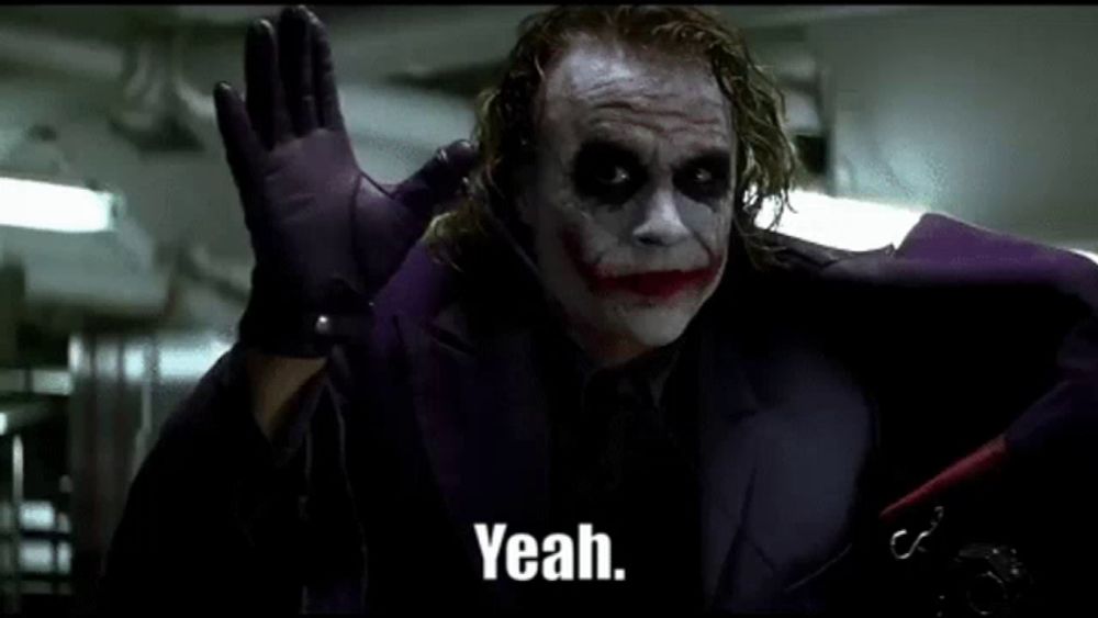 the joker is wearing a purple suit and gloves and waving his hand .