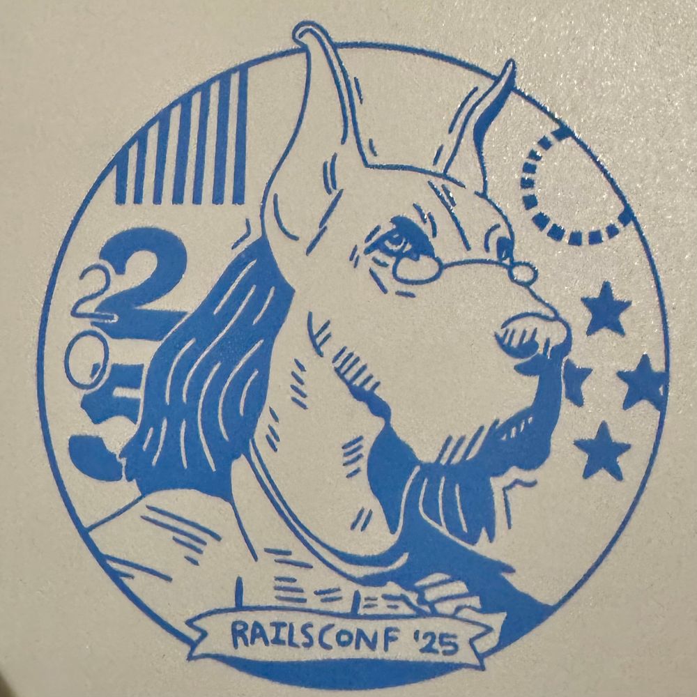 Detail of a notebook cover with printed illustration of a dog, with hair, glasses, and clothes resembling those of Ben Franklin. A small banner at the bottom reads “railsconf ‘25”. 