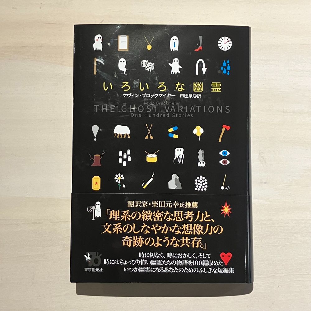 書影。黒い地にサイコロや太鼓や振り子などいろいろな絵がアイコンが並ぶように描かれる。それらの中に様々な格好の幽霊が混ざっている。