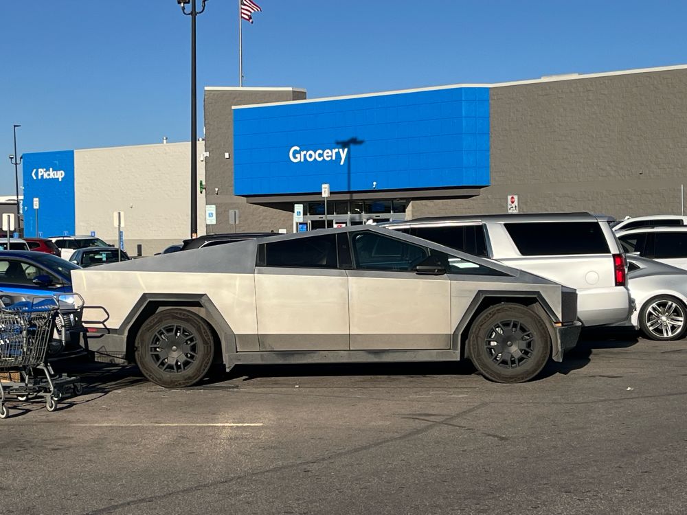 Right side profile of a Tesla Cybertruck in a Walmart parking lot. The vehicle itself is a bit dirty. 