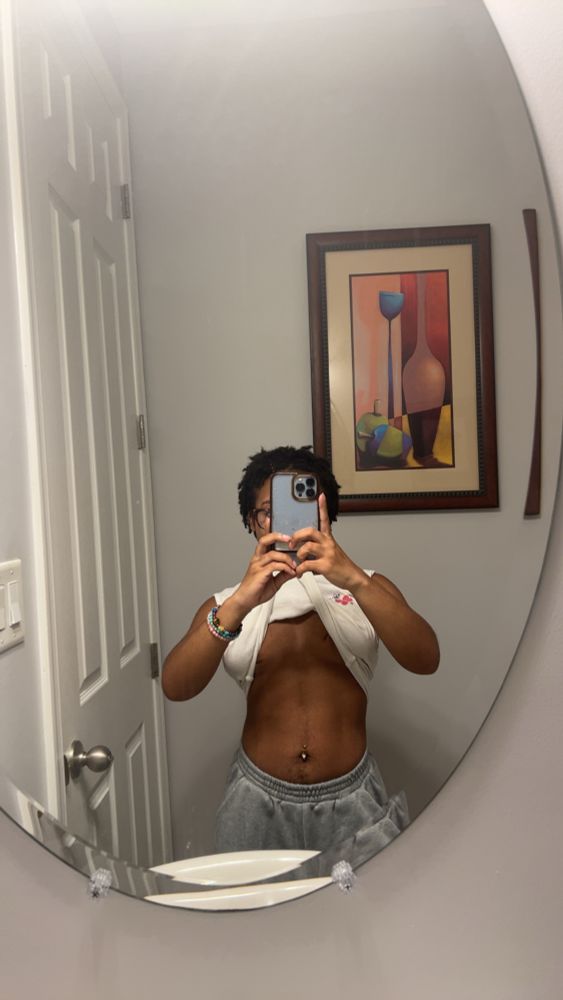 Elijah taking a mirror selfie, his phone is in front of their face and he has the bottom of his shirt in their mouth to hold it up and show his tummy. He’s wearing sweats