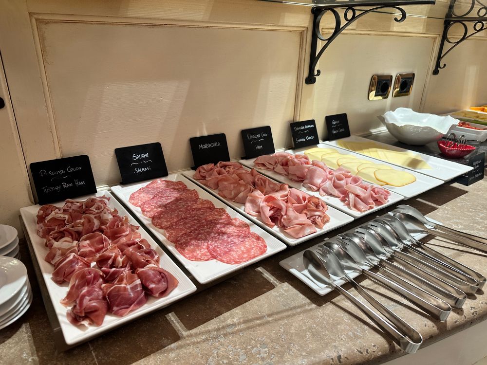 The display of cured meats and cheeses at a hotel breakfast buffet. Options include prosciutto, salami, mortadella, ham, smoked provolone, Gouda, and a bowl of fresh buffalo mozzarella.