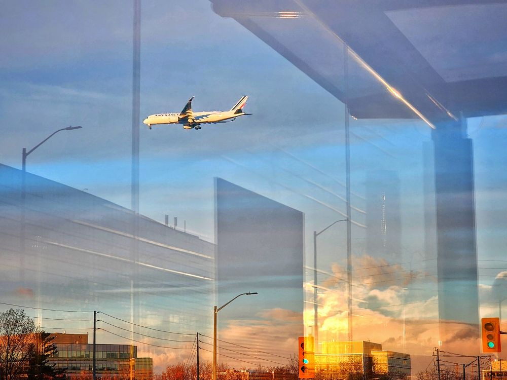 An Air France jumbo passes over Eglinton Avenue as it descends towards Toronto Pearson International Airport. Reflections of the setting sun and surrounding buildings are seen in the glass of the bus shelter where the photo was taken. 