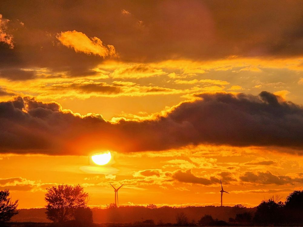 The setting sun dips beneath a line of clouds and above wind turbines in West Lincoln Ontario