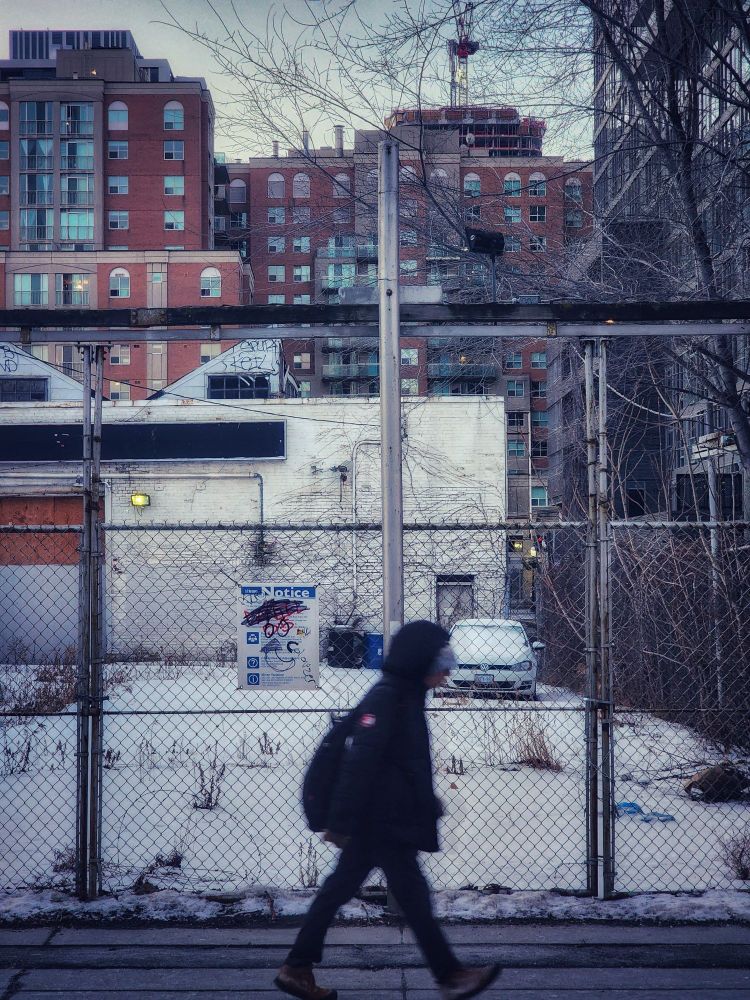 A pedestrian walks along Queen Street East in the Moss Park neighbourhood of Toronto Ontario in front of an abandoned car repair garage. 