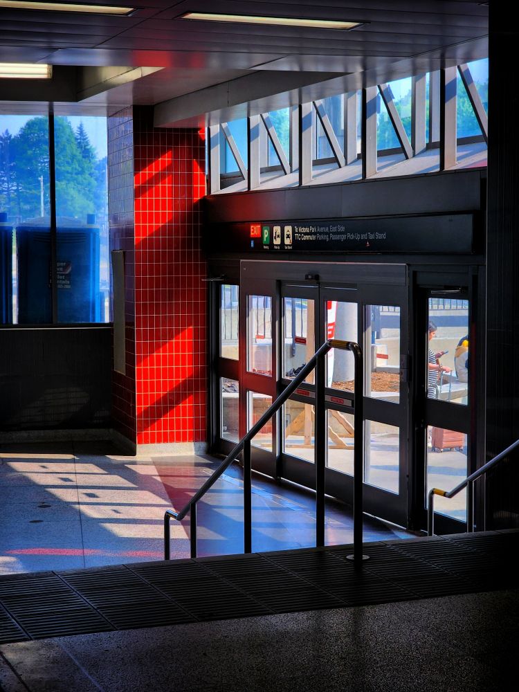 A red-tiled column and shadows of the exit doors on the floor beside the exit to Victoria Park Avenue from Victoria Park Station in Toronto 