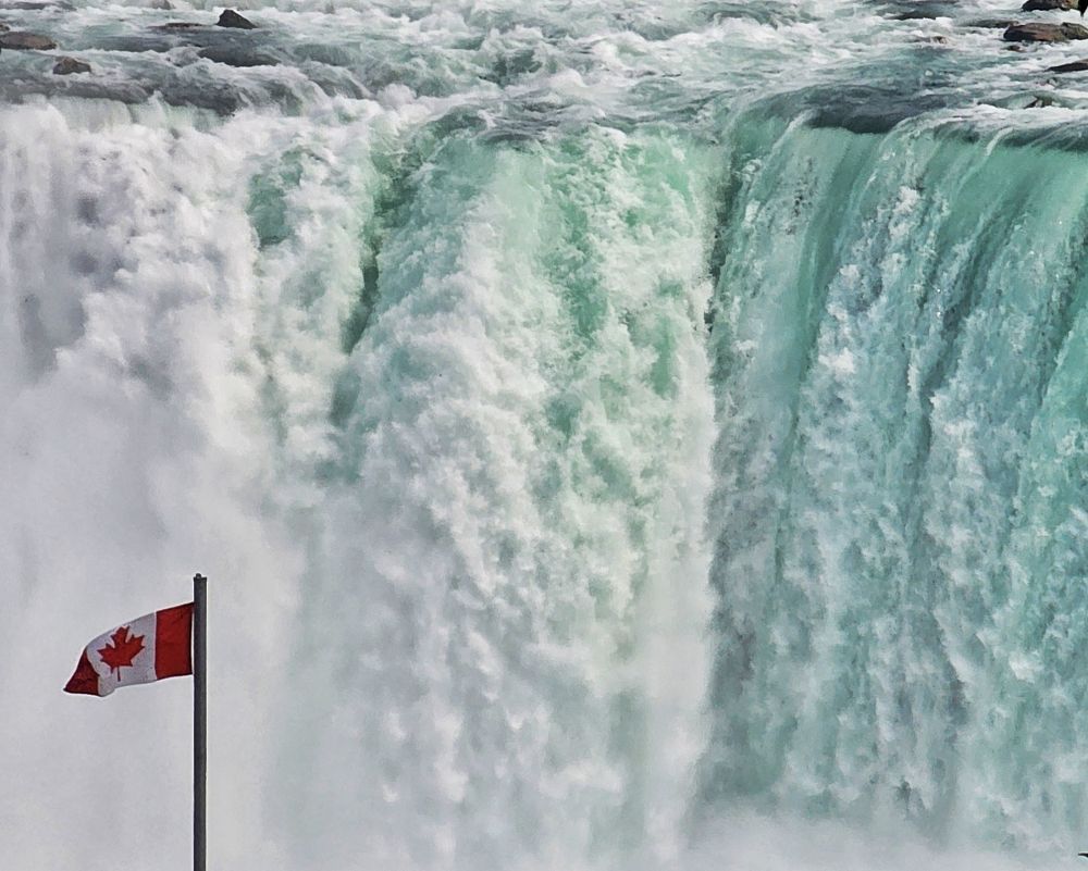 Water thunders over the Horseshoe Falls at Niagara Falls Ontario. A Canadian flag stands proudly in the way, I mean foreground.