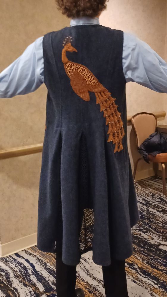 A knee length wool vest, appliqued with a peacock in rust colored suedecloth, inspired by the Peacock Doors at the Palmer House in Chicago, made from cast bronze by Tiffany in the 1880s.  Modeled here by one of my male colleagues, showing that this piece works well on any gender.  All materials in this piece were recycled from previously owned sources with the exception of the square studs in the peacock's tail.