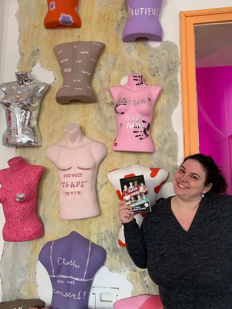 A white woman holding a black book in front of a wall of manicans