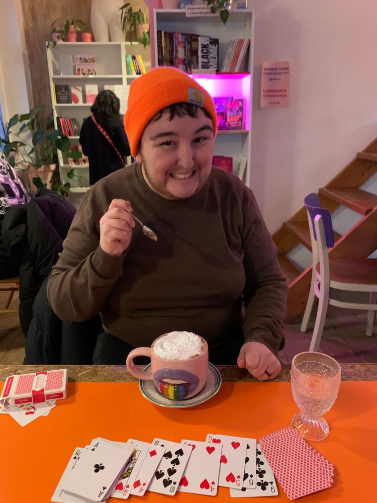 A person with an orange hat smiling with a rainbow mug