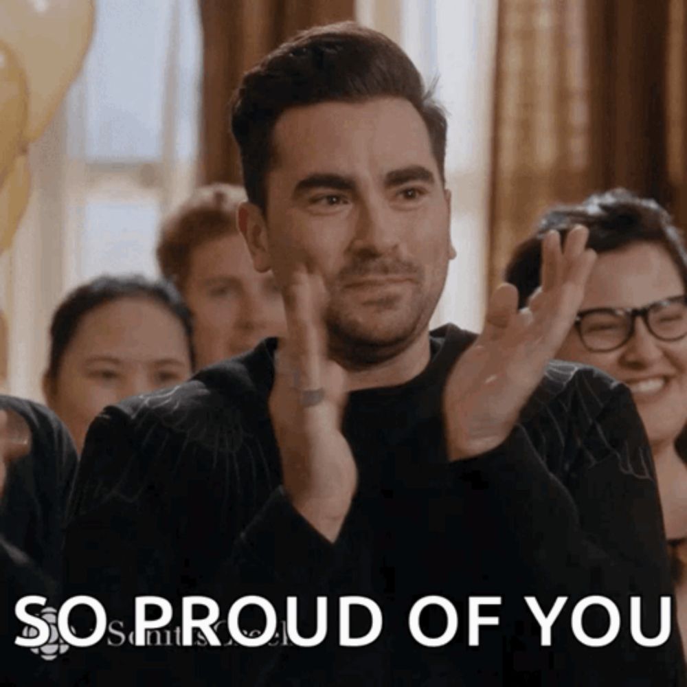 a man applauds in front of a sign that says " so proud of you "