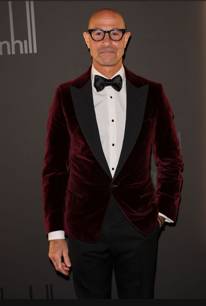 Stanley Tucci in a claret-colored velvet tuxedo jacket with black lapels and trousers, white shirt, black buttons, satin bow tie. 